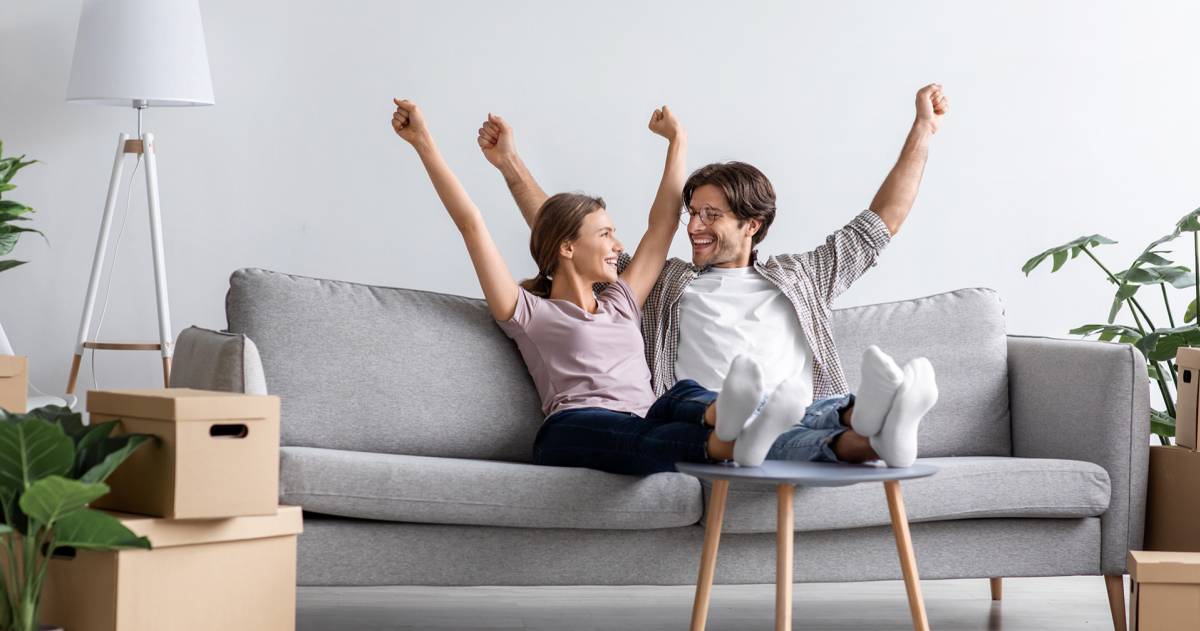 Jong stel dat samen is gaan wonen en op de bank zit met de armen omhoog van blijdschap