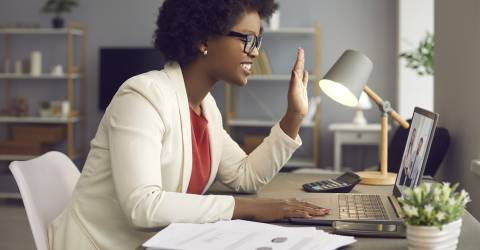 Vrouw thuis aan het werk en zwaait achter laptop naar videocall
