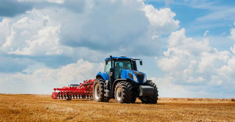 Een blauwe tractor is het land aan het omploegen met een mooie lucht op de achtergrond